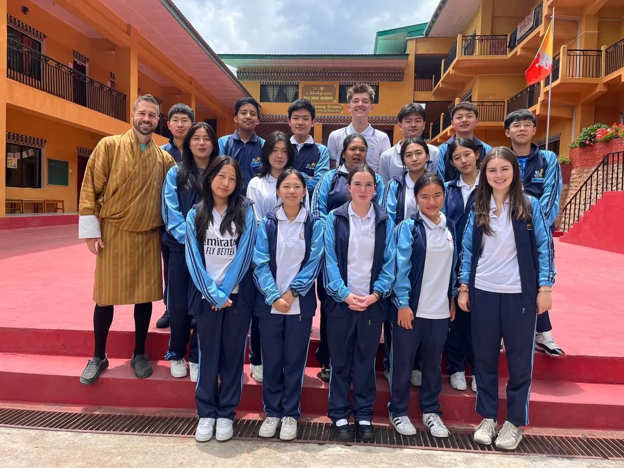 A cohort of visiting exchange students standing with their ELC classmates and a teacher in gho on the school courtyard steps