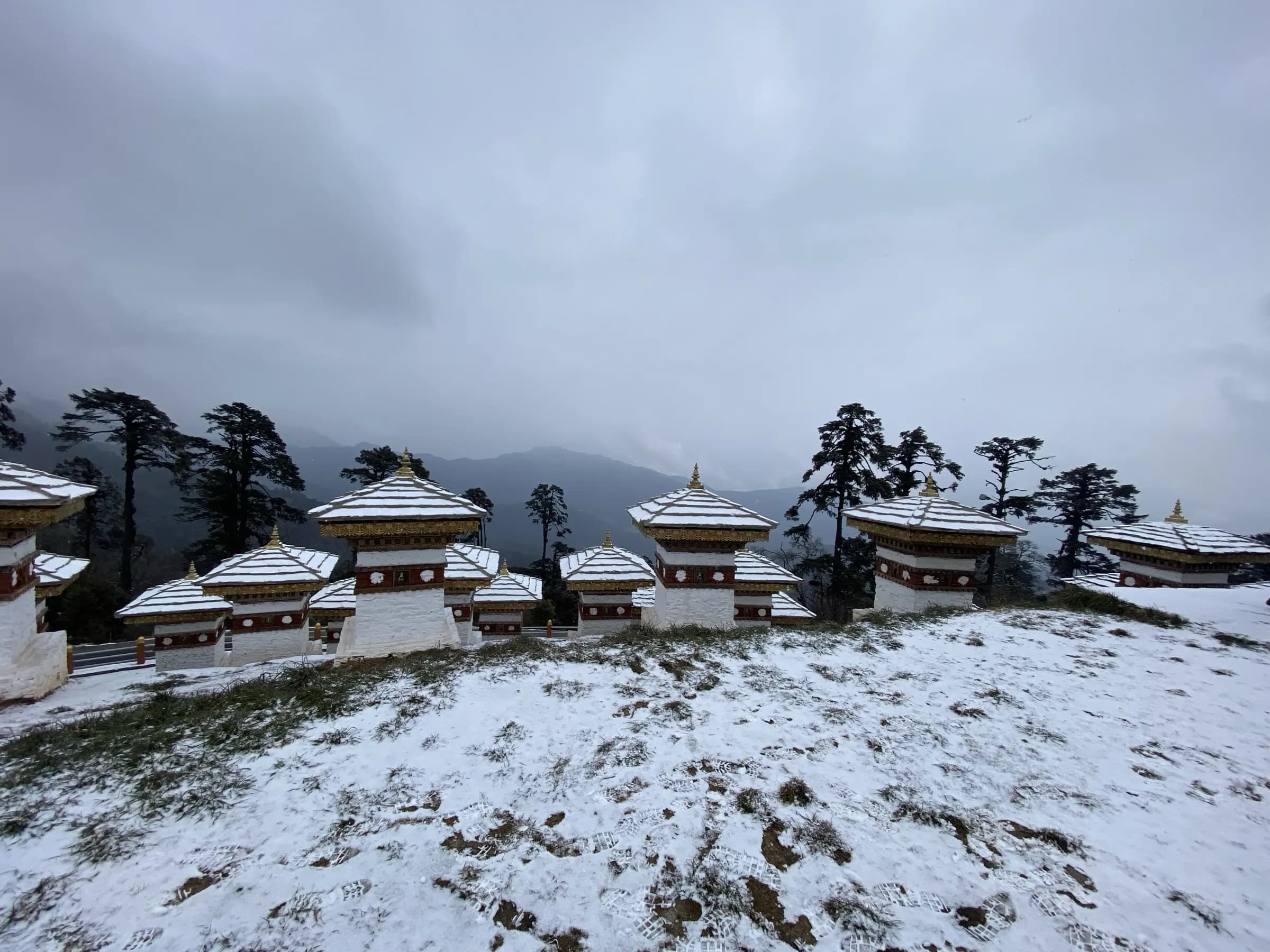 The 108 chortens at Dochula Pass under fresh snow, dark pines and the Himalayan ridgeline behind them