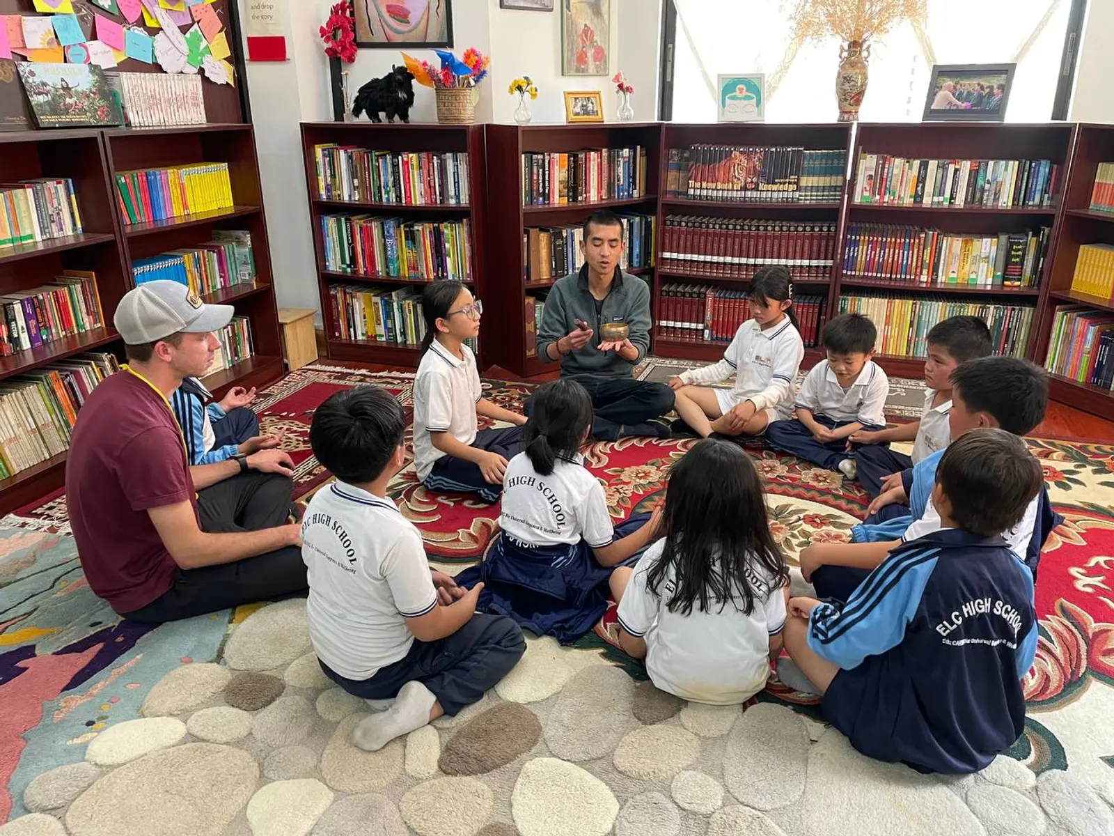 Children sitting in a circle on a patterned rug in the ELC library with a teacher leading the session