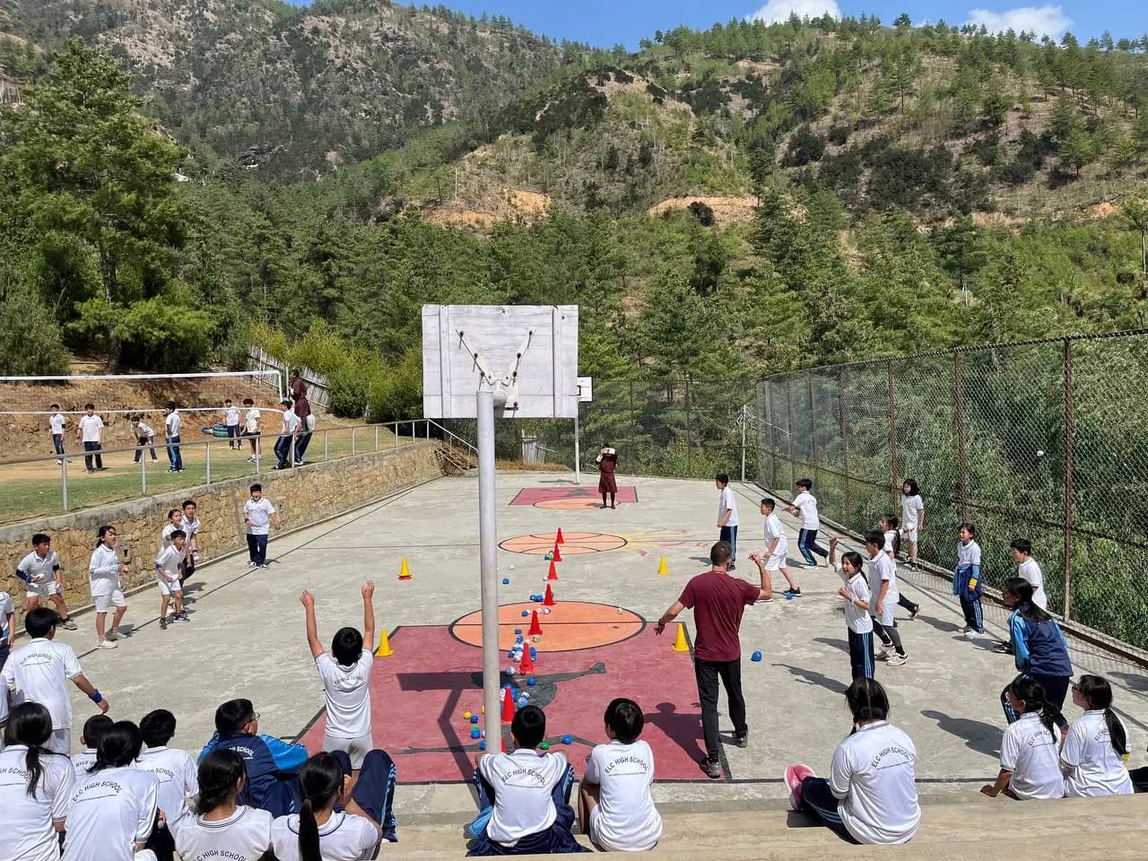 An ELC games period on the outdoor court, the whole class taking part, with forested hills behind