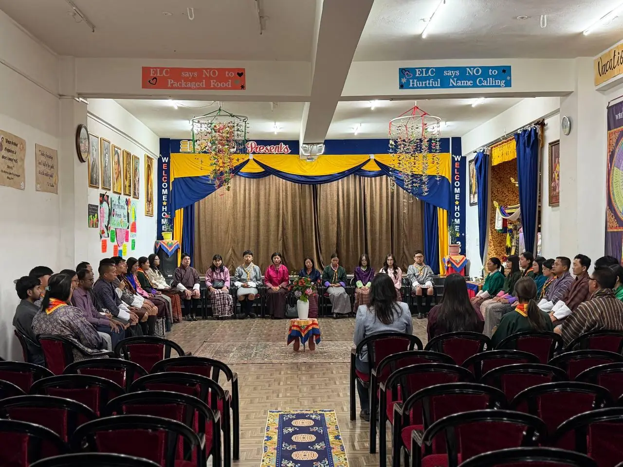 ELC staff seated in a circle at the front of the school hall, beneath banners reading ELC says NO to Packaged Food and ELC says NO to Hurtful Name Calling